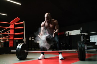 an african american man sprays magnesium or talcum powder with his palms before lifting a barbell. heavyweight preparing for competition.