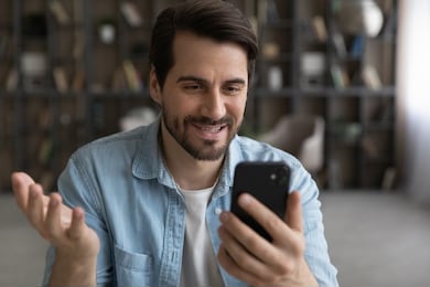 smiling young caucasian man look at smartphone screen talk on video call on modern gadget. happy millennial male client or user have webcam digital virtual conference on cellphone at home.