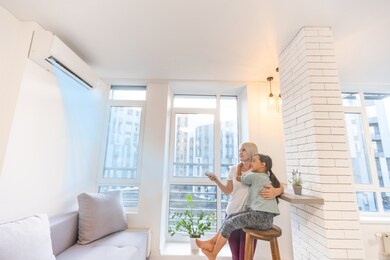 happy family under air conditioner, mom holding remote control switch on conditioning in living room adjust comfort temperature for daughter, climate system at modern home