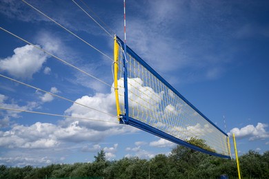a beach volleyball net against a bright blue cloudy sky.