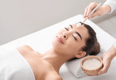 beauty treatment. professional beautician applying clay mask to asian woman at spa salon, young attractive korean female lying on massage table, enjoying face care procedures, closeup shot, free space