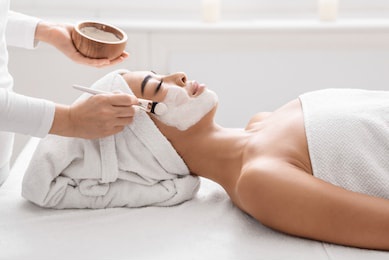 skin lifting treatment. young asian woman getting facial nourishing mask by professional beautician at spa salon, calm lady enjoying wellness day and beauty procedures, side view with copy space