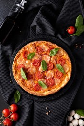 homemade pizza with mozzarella and cherry tomatoes on a black round board, top view