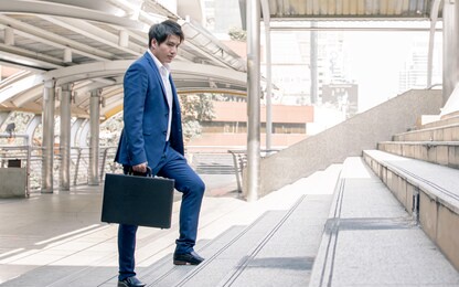 focusing on business man wearing blue formal suit, holding briefcase, hurry and rush running on the steps while going to work in the early morning