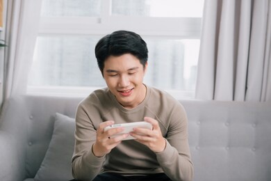 man playing online games with a smart phone sitting on a couch at home