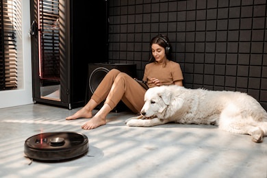 robot vacuum cleaner cleans the floor with a woman sitting with her dog at home studio. concept of smart home appliances and automatic cleaning