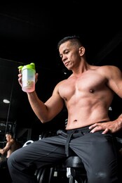 a fit asian man checks out remaining sports drink after a vigorous workout. gym or fitness club setting.
