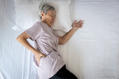 sad asian senior woman touching hip on her bed,problem of pain while sleep feel backache discomfort,female old elderly suffering from sudden back pain caused by uncomfortable mattress in the bedroom