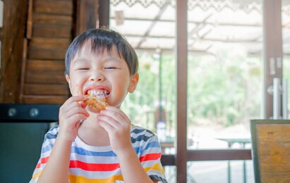 cute asian kid boy eating fried chicken by self. copy space. soft focus.