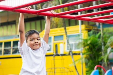 kid exercise for health and sport concept. happy asian student​ child boy playing and hanging from a steel bar at the playground. 6-7 years old.