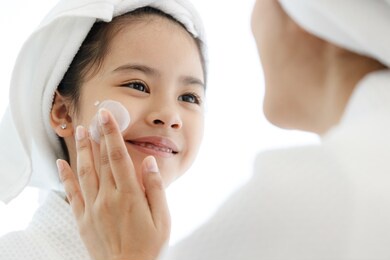 mother adding treatment cream on the cheek to young and cute asian girl with spa dress and head covered with a white towel.