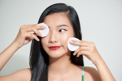 healthy fresh asian girl removing makeup from her face with cotton pad smiling. 