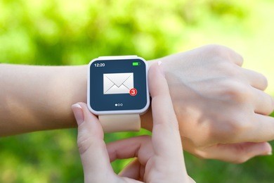 isolated female hands with white smartwatch with email on the screen on a background of green grass
