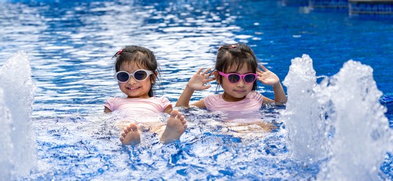 portrait of pretty asian twins smilling and posing on swimming pool background wearing pink swim suit and sun glasses