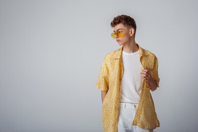 young fashionable guy wearing trendy sunglasses, yellow shirt, white t-shirt, trousers. summer fashion conception, studio portrait. copy, empty space for text