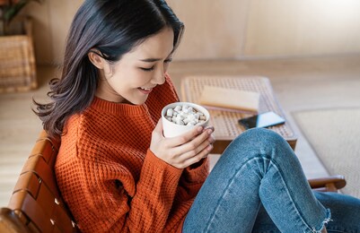 young beautiful asian woman in sweater hands holding a cup of coffee morning winter time relax at home. happy cheerful relaxing in cold winter, barista lifestyle concept banner