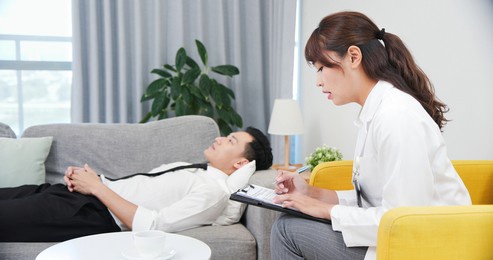 asian female psychologist has consultation with male patient who is lying on sofa