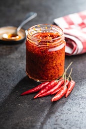 red hot chili paste and chili pepper in jar on black table.