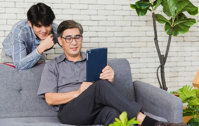 asian senior businessman with digital tablet discuss together with young team in office. father man and his son sit on sofa talking chatting on video call conference on tablet in living room at home