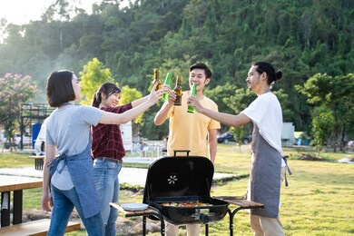 group of asian man and woman are having new year party outdoor in the evening together. friends are drinking bottle of beer and drinking with happiness and smile. travel nature, camping on camper van.