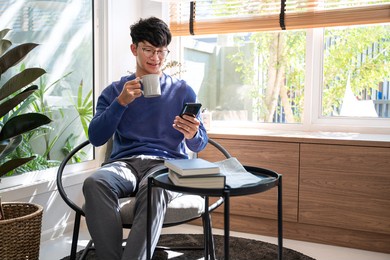 handsome asian teenager man wearing casual clothes in glasses using smart phone browsing internet on mobile phone device at the living room 