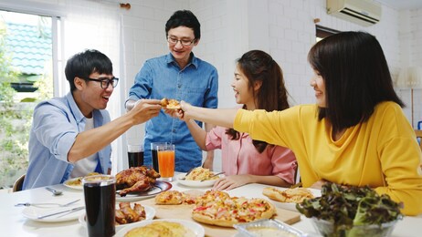 happy young friends group having lunch at home. asia family party eating pizza food and laughing enjoying meal while sitting at dining table together at house. celebration holiday and togetherness.