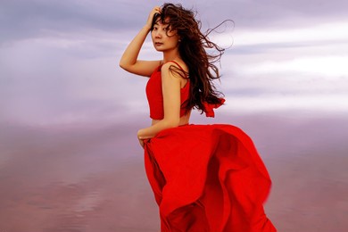 elegant asian woman in red silky dress walking by a salt fantastic lake at sunset in wind.