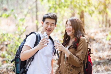 young asian man and woman couple with backpack drinking water during travel in forest, couple travel concept.