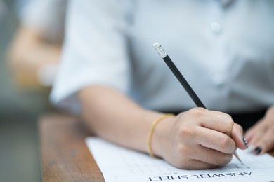 selective focus of the teenage college students sit on lecture chairs do final examination and write on examination paper answer sheets in the classroom. university students in uniform in classroom.