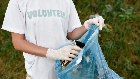 clean up day. cropped shot of a young woman volunteer wearing uniform and rubber gloves with trash bag in hands cleaning forest or park from garbage. ecology problems and nature pollution