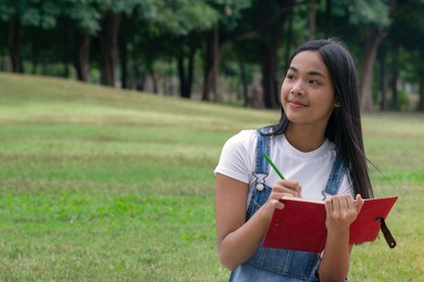 teenage asian girl sat on the lawn looking at something and holding a notebook in her hand., enjoy and relax in summer