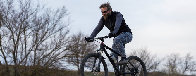 sports brutal bearded guy on a modern mountain bike. cyclist on the green hills in the spring.