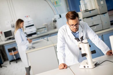 handsome young scientist in white lab coat working with binocular microscope in the material science lab