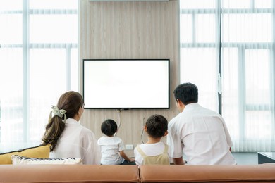 asian happy family sitting and watching television in living room at home and spent quality time together for activity in vacation day, holiday, happiness or lifestyle concept.
