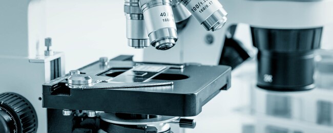 science microscope on lab bench. microbiology laboratory. blue toned image of binocular microscope