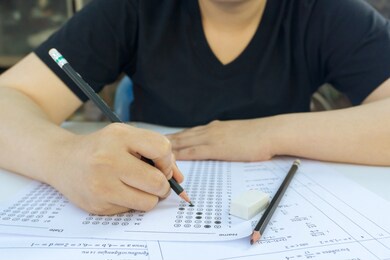 woman students hand holding pencil writing selected choice on answer sheets and mathematics question sheets. students testing doing examination. school exam