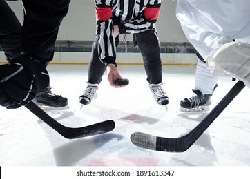 hockey referee with puck standing on ice rink with two rivals with sticks on his right and left waiting for moment to shoot it