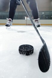 legs of male hockey player in sports uniform and skates standing on ice rink against stadium environment while going to shoot puck