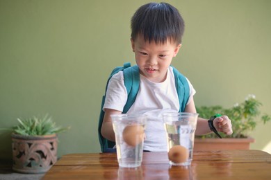happy smiling excited little asian school kid studying science, doing fun and easy floating egg science experiment to learn about the density of salt water effect to floating and sinking of the eggs