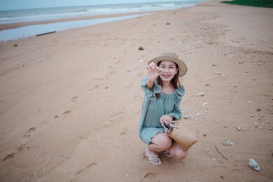 asian woman in green dress sitting away with rain sky on the beach by the sea.
