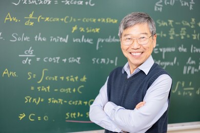 asian senior male professor smile at you in front of blackboard with calculus formula at college classroom