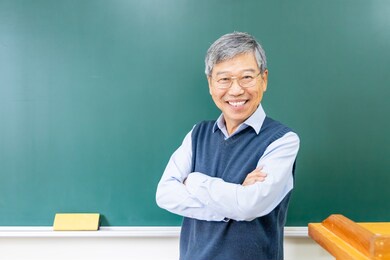 asian senior male professor arm crossed and smile at you in front of blackboard at college classroom