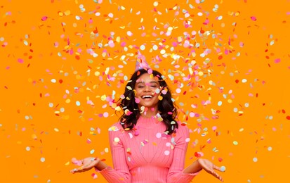 happy birthday! cheerful funny young ethnic woman with festive confetti on yellow background