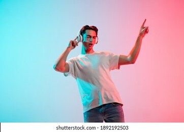 listening to music, dancing. young caucasian man's portrait on gradient blue-pink studio background in neon. concept of youth, human emotions, facial expression, sales, ad. half length, copyspace.