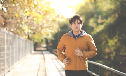 asian man in yellow hoodie jogging and running beside road in park at autumn morning. 