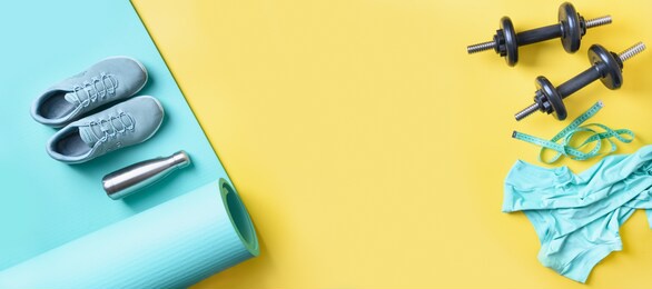 banner of sport and fitness equipment, female tee-shirt, yoga mat, shoes, water bottle on yellow. banner with copy space. view from above.