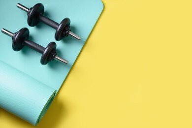 sport black dumbbells on turquoise yoga mat on yellow background. copy space. flat lay. view from above.