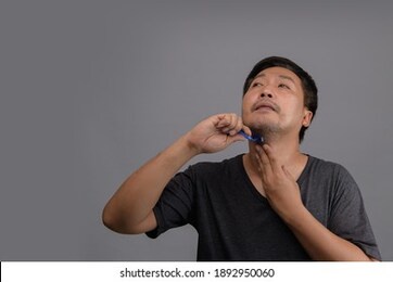 close up portrait of a asian meddle aged man shaving beard with razor isolated over gray background. free from copy space for text.