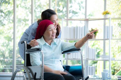 asian elderly mother who sitting on wheelchair and wearing red headscarf, show her lovely daughter to look at something through window very happily and smile after she survive from cancer or leukemia.