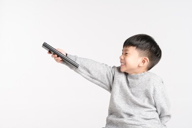 asian boy about 5 years old holding tv remote with happy smile on white background